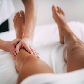 Physiotherapist massaging female patient with injured leg. Sports injury treatment.